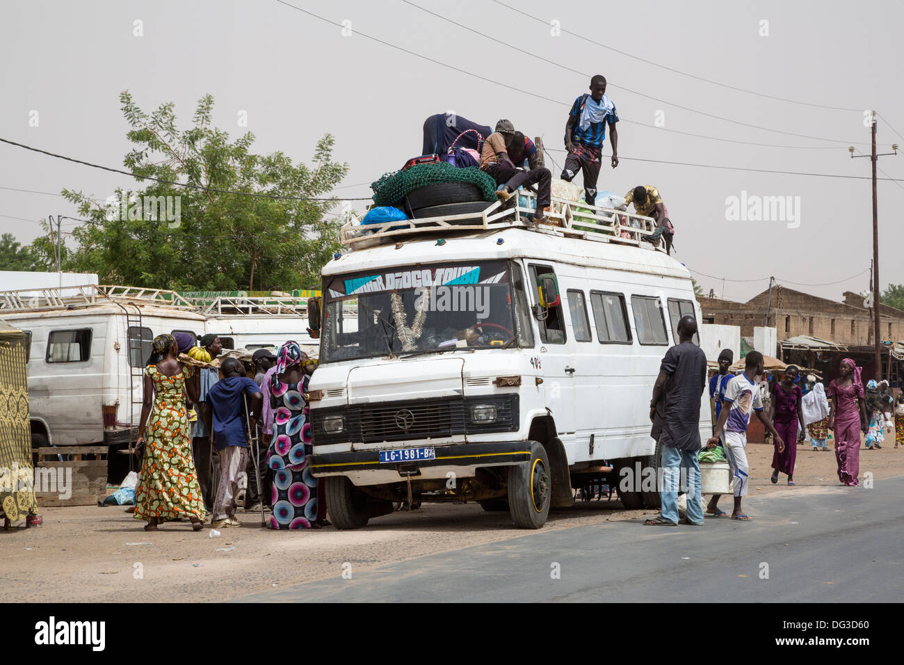 Il Senegal, Touba. Il trasporto locale e la sicurezza del traffico. Giovani uomini caricare le merci sulla sommità; alcuni passeggeri si ride vi. Foto Stock
