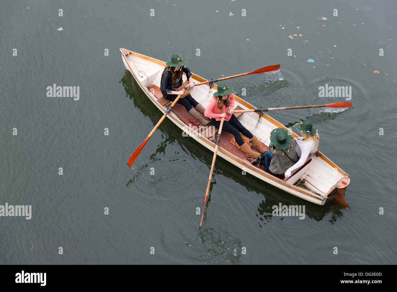 Tre giovani donne remare una barca sul fiume, indossando cappelli australiani. Vista aerea Foto Stock