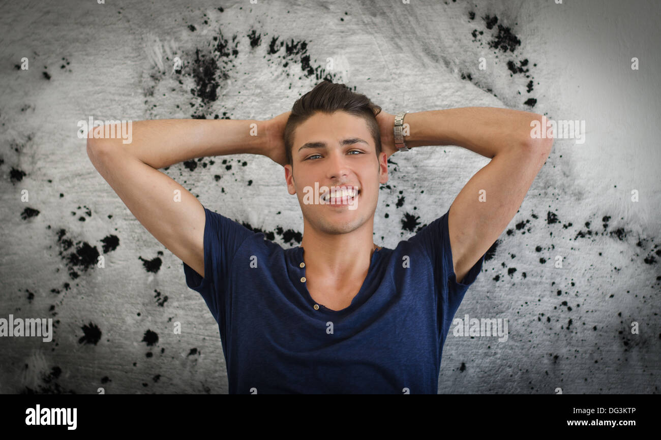 Bello e fiducioso giovane uomo sorridente con le braccia in alto, macchiato il muro dietro di lui. Foto Stock