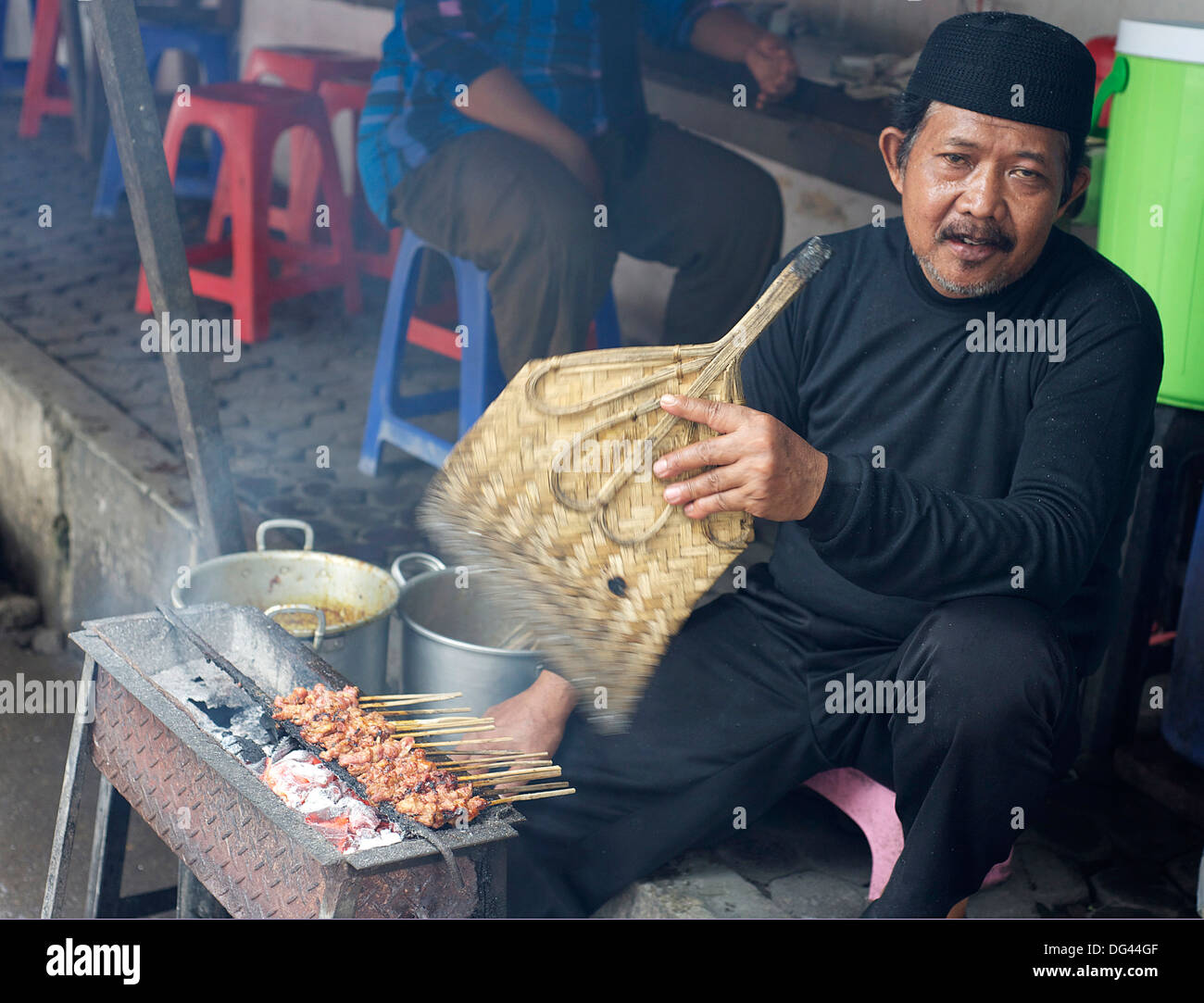 Uomo musulmano nel mercato per la cottura il pollo satay, fanning il carbone di legna con una foglia di palma ventilatore, Solo, Java, Indonesia, sud-est asiatico Foto Stock