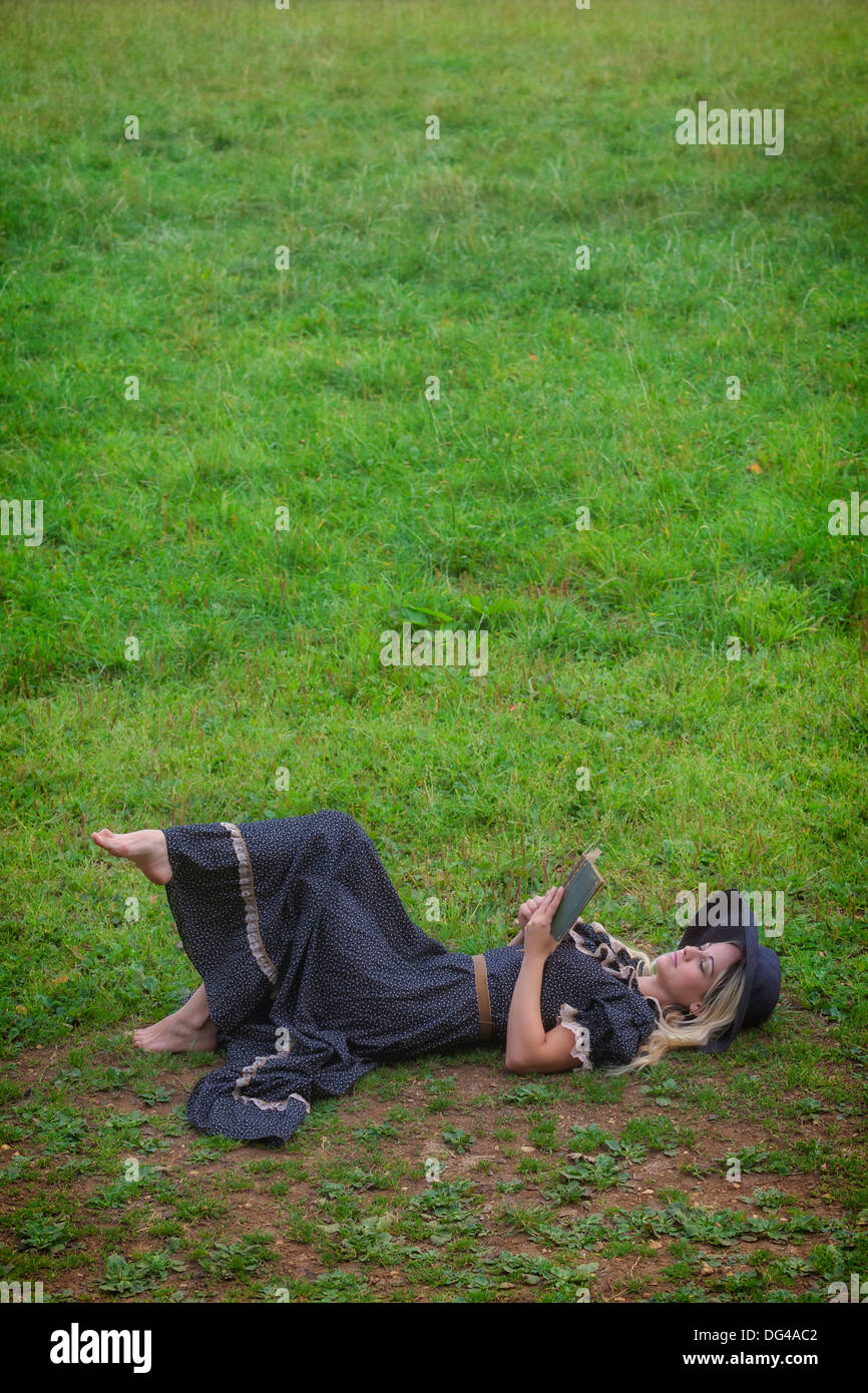 Una donna in un romantico abito è sdraiato su un prato, la lettura di un libro Foto Stock