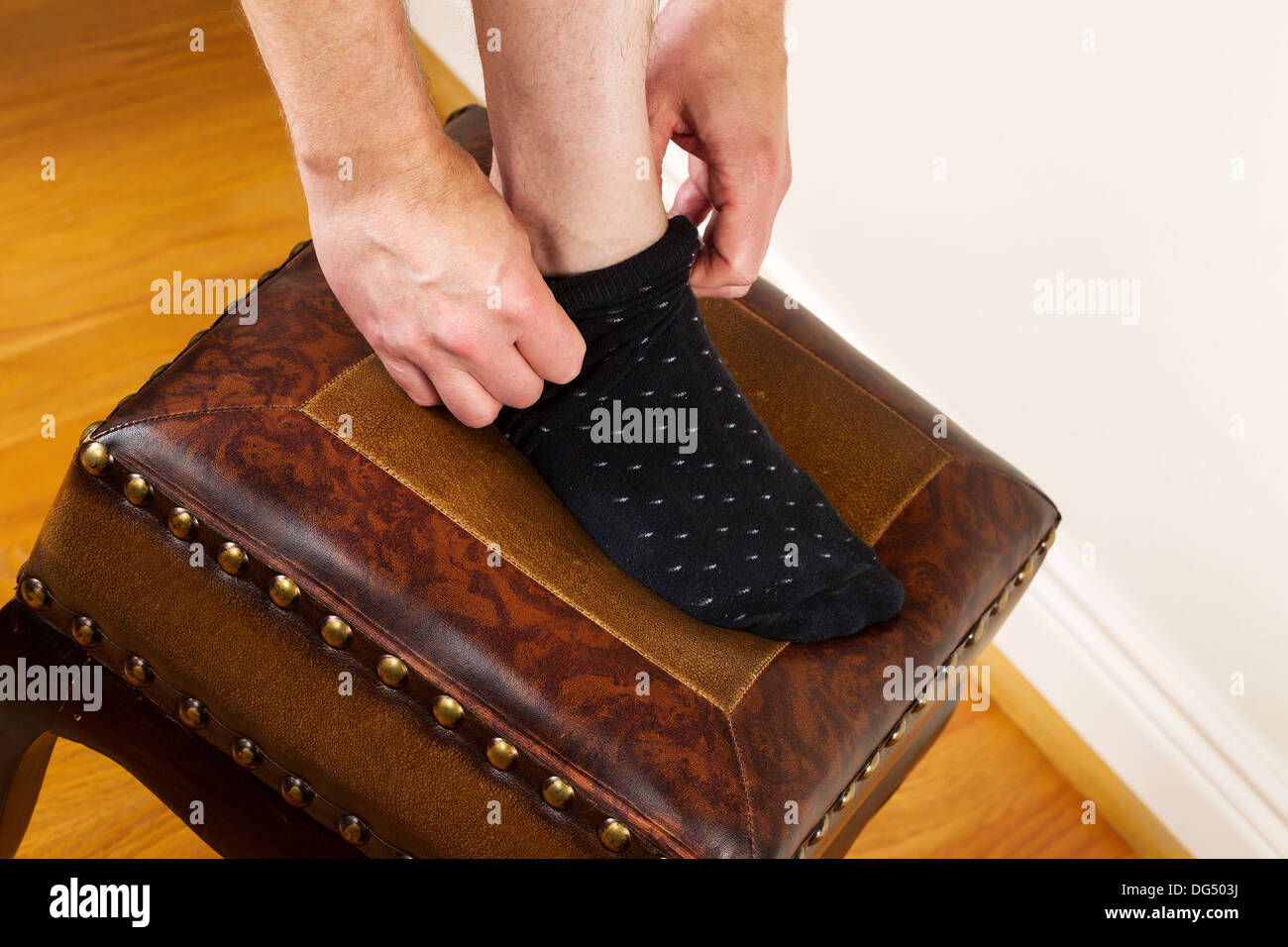 Foto orizzontale dell'uomo tirando verso l'alto abito calzino appoggiando il piede sul piede imbottito Sgabello rosso con pavimenti in legno di quercia Foto Stock