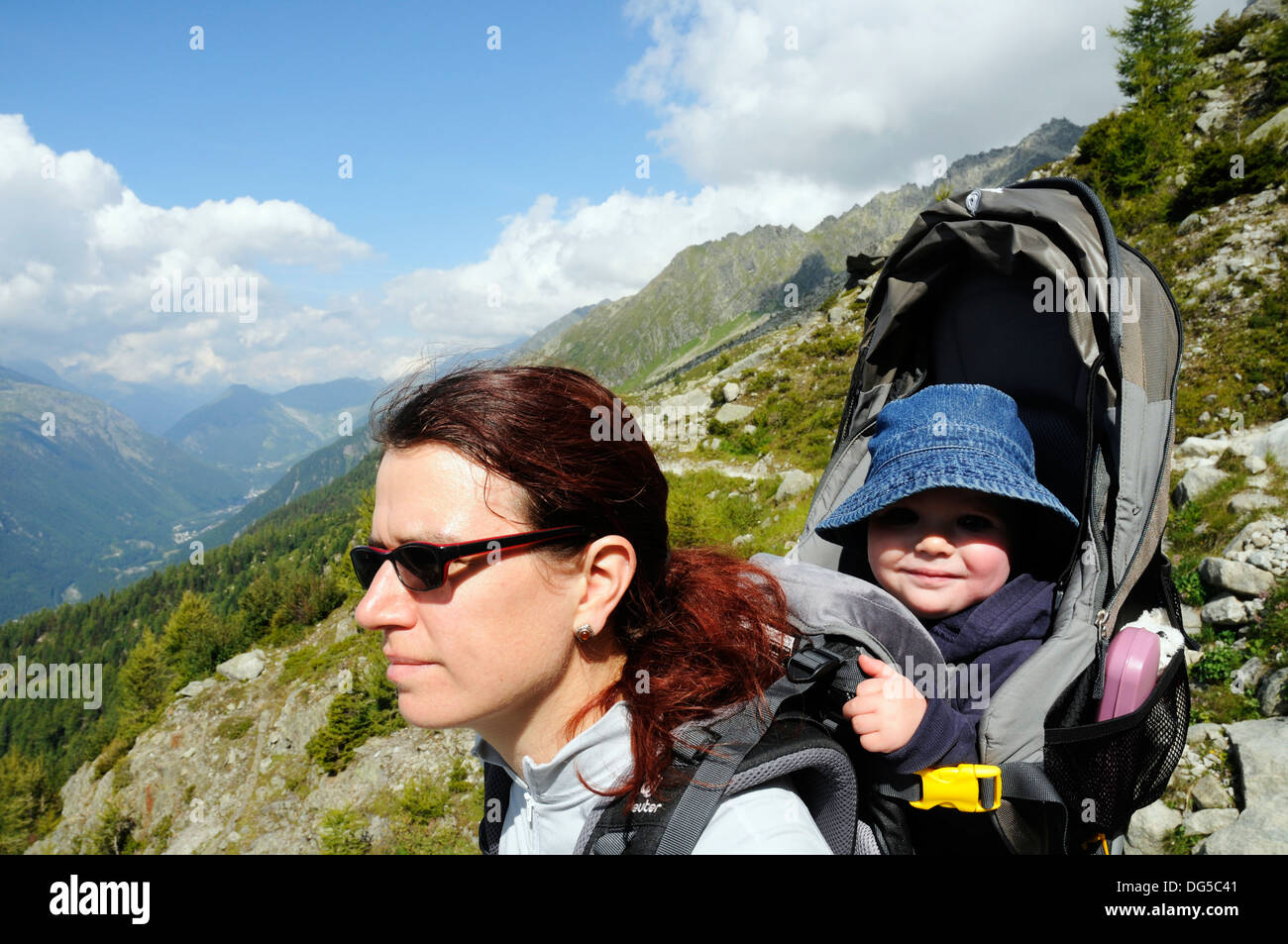 Una madre escursionismo nelle Alpi francesi che porta il suo bambino in una baby carrier Foto Stock