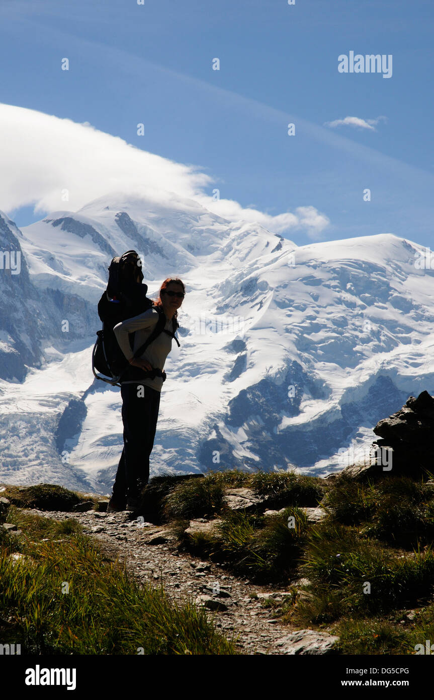 Una madre escursionismo nelle Alpi francesi che porta il suo bambino in una baby carrier con Mont Blanc dietro Foto Stock