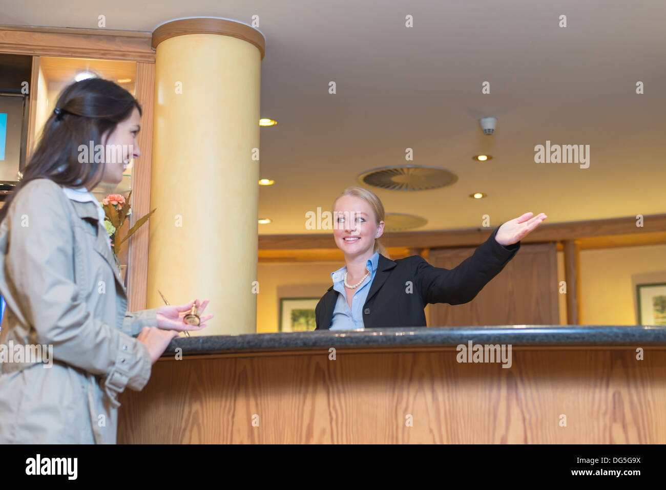 Basso angolo di visione di un bellissimo Friendly receptionist sorridente dietro il service desk nella hall di un hotel aiutando una femmina di valutazione Foto Stock