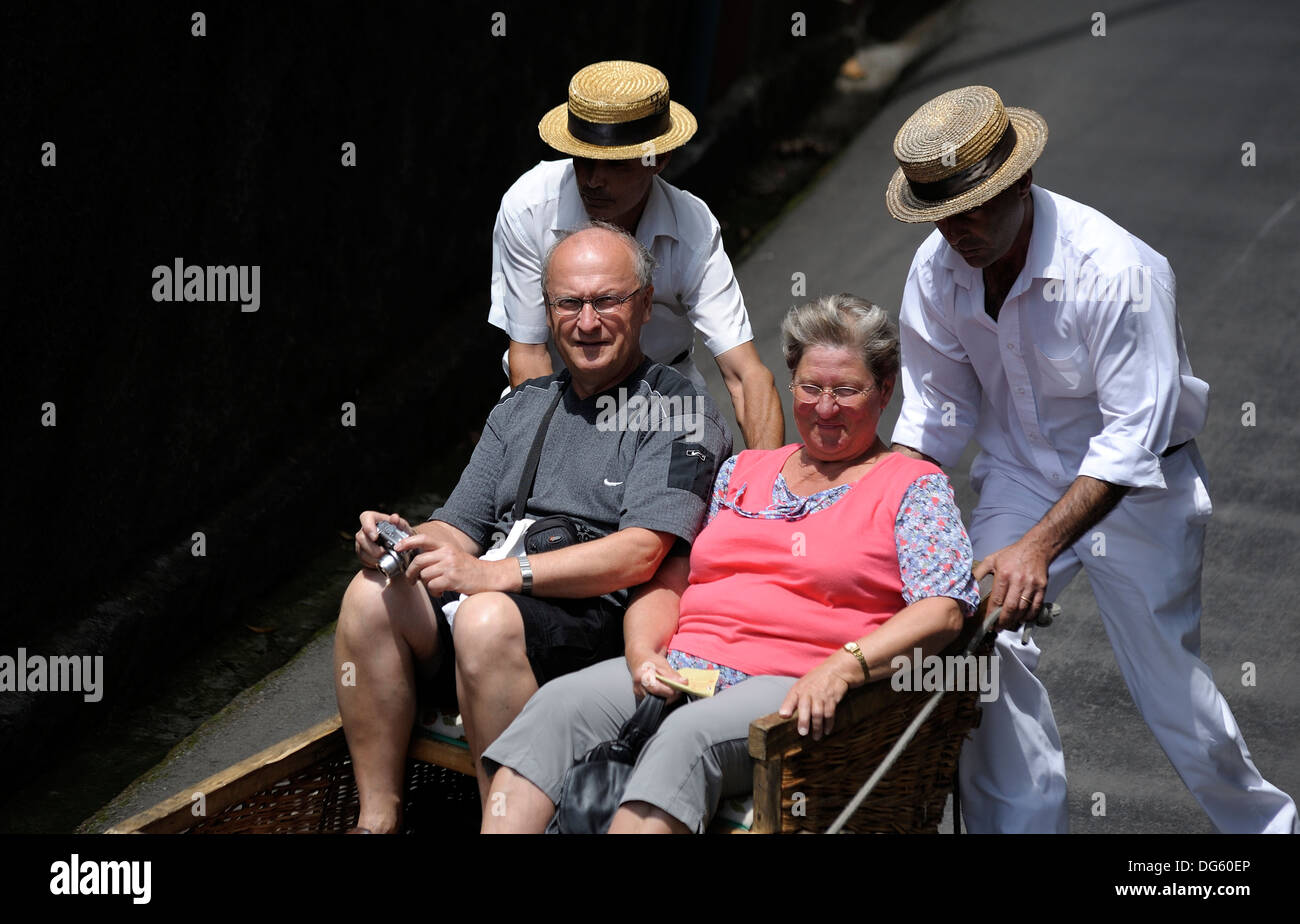 Monte di Madera, due Carreiros de Monte alla guida di una pista da slittino con 2 turisti a bordo per il viaggio di ritorno verso il basso a Funchal Foto Stock