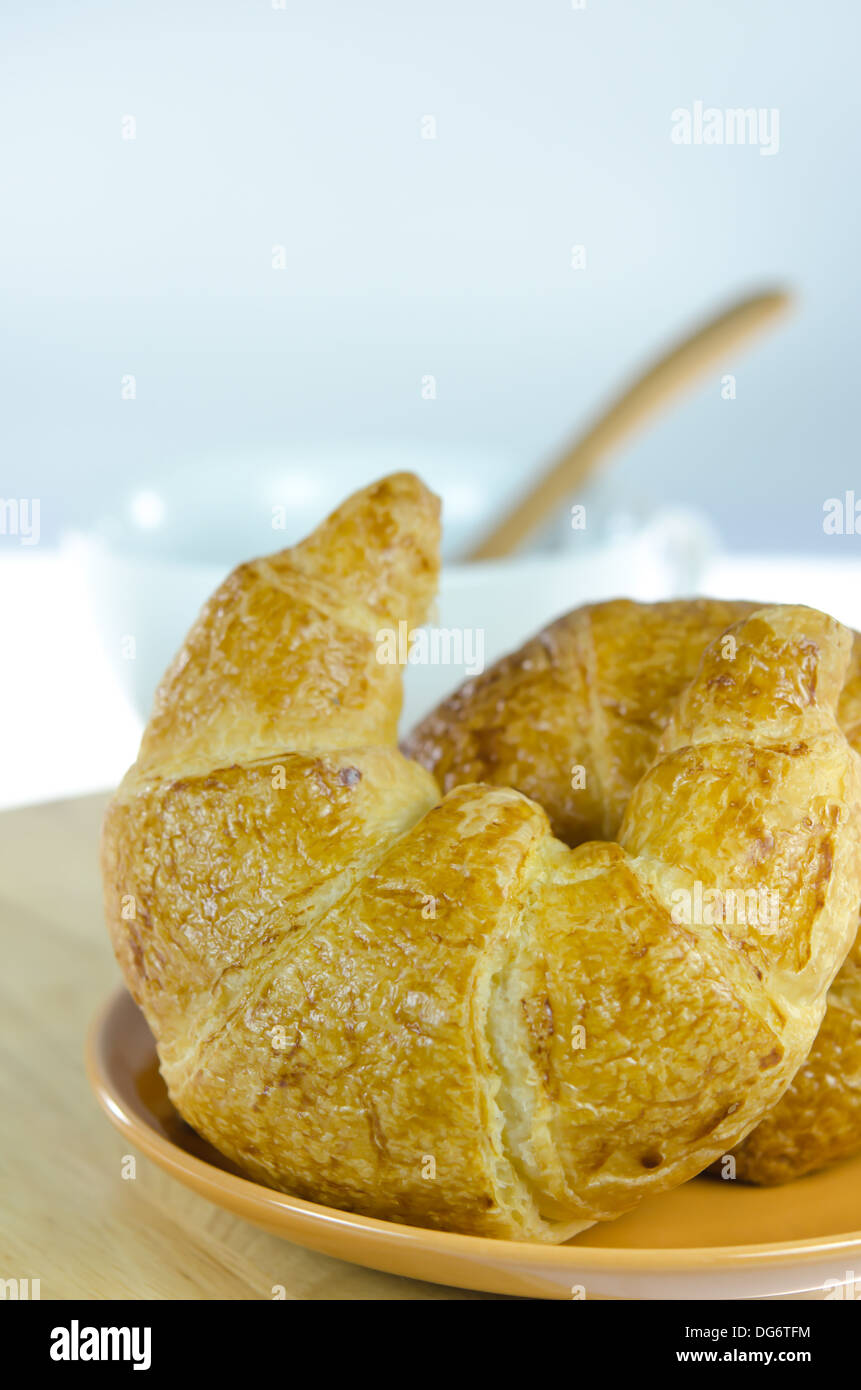 Close up croissant sul piatto marrone e bianco una tazza di caffè con cucchiaino , cibo fresco Foto Stock