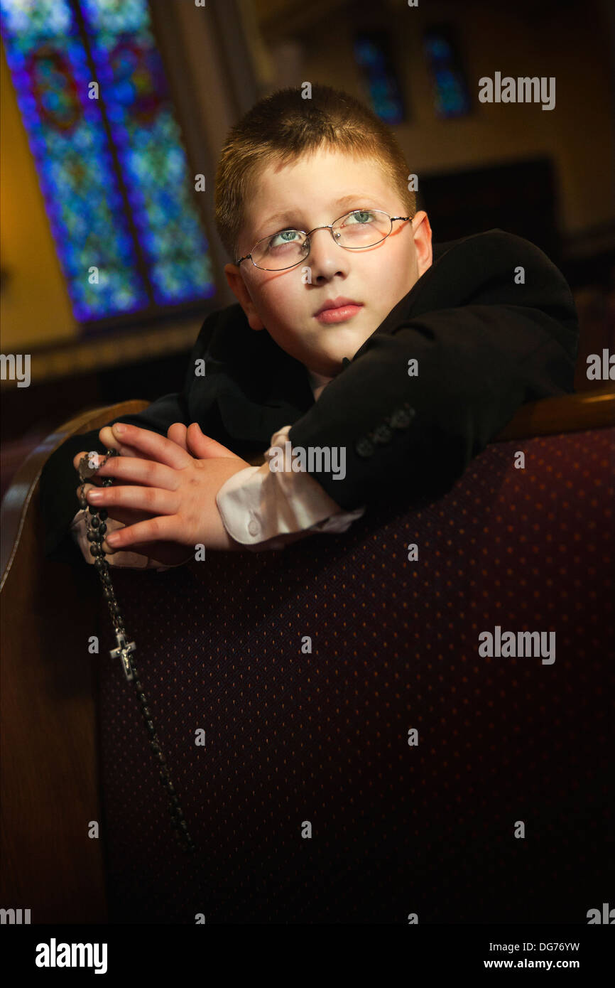 Un giovane ragazzo caucasico alza lo sguardo al cielo mentre egli prega in chiesa Foto Stock