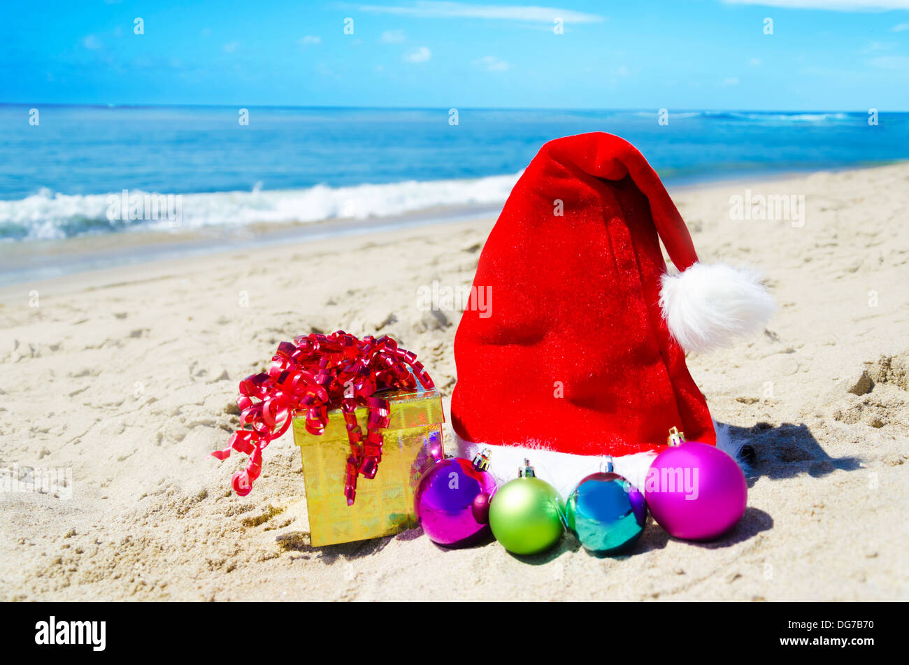 Cappello di natale con confezione regalo e palle di Natale sulla spiaggia dall'oceano - Concetto di vacanza Foto Stock