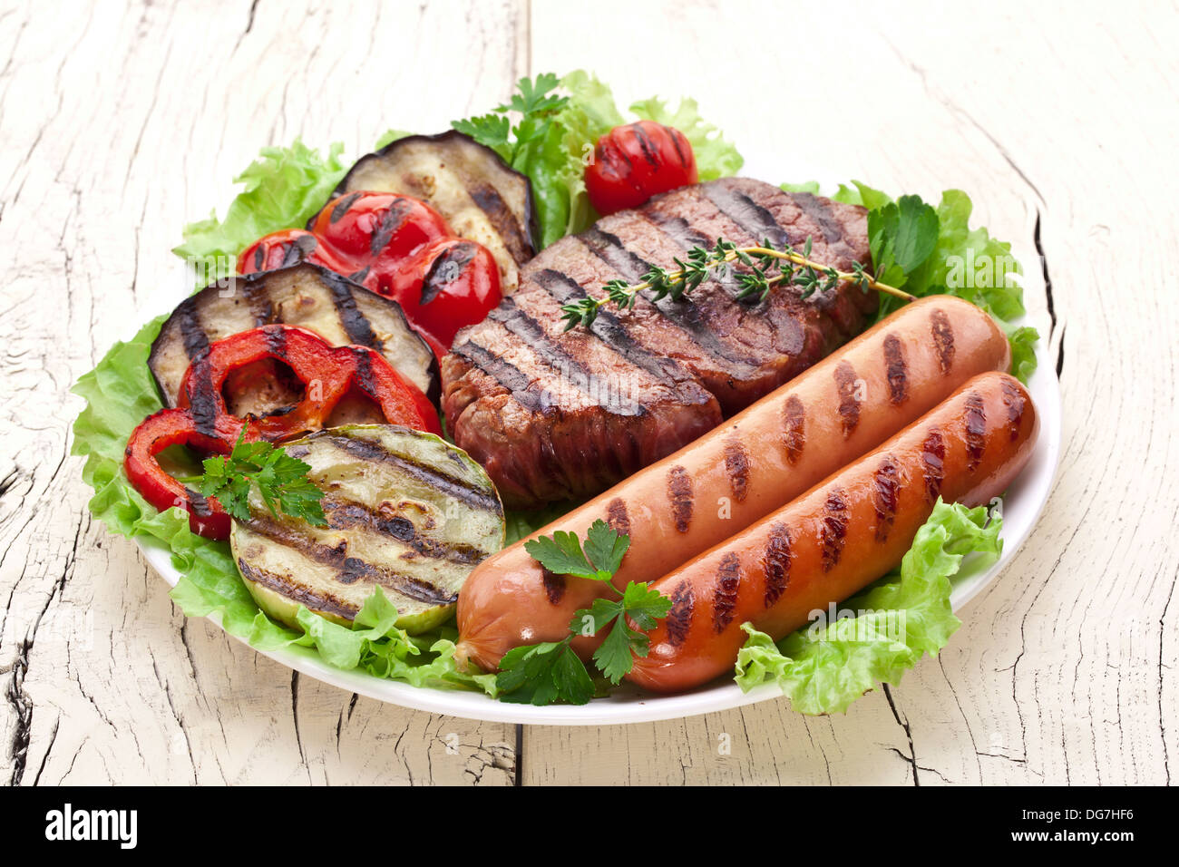 Bistecca alla griglia,salsicce e verdure sopra le foglie di lattuga su un tavolo di legno. Foto Stock