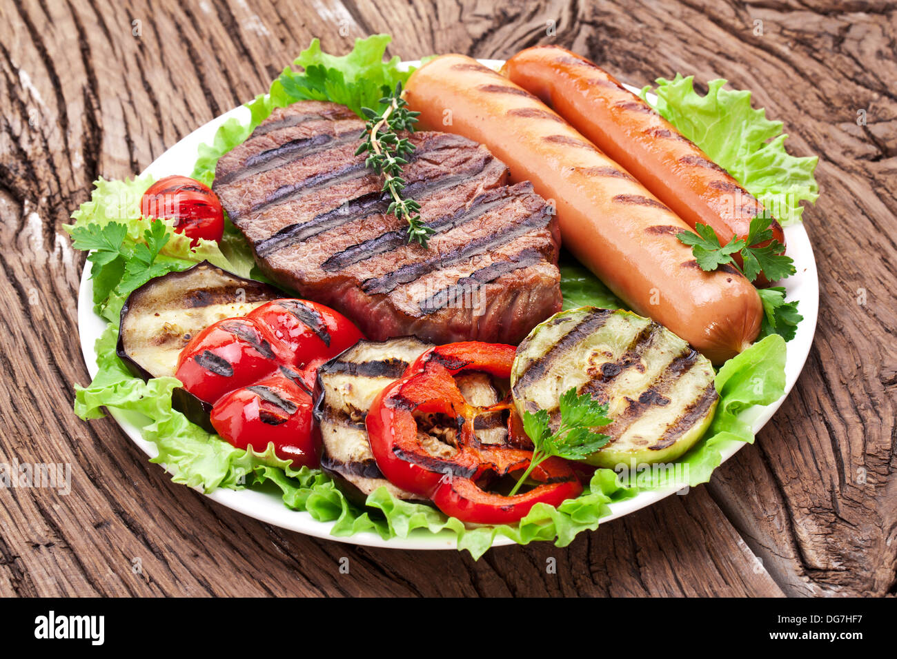 Bistecca alla griglia,salsicce e verdure sopra le foglie di lattuga su un tavolo di legno. Foto Stock