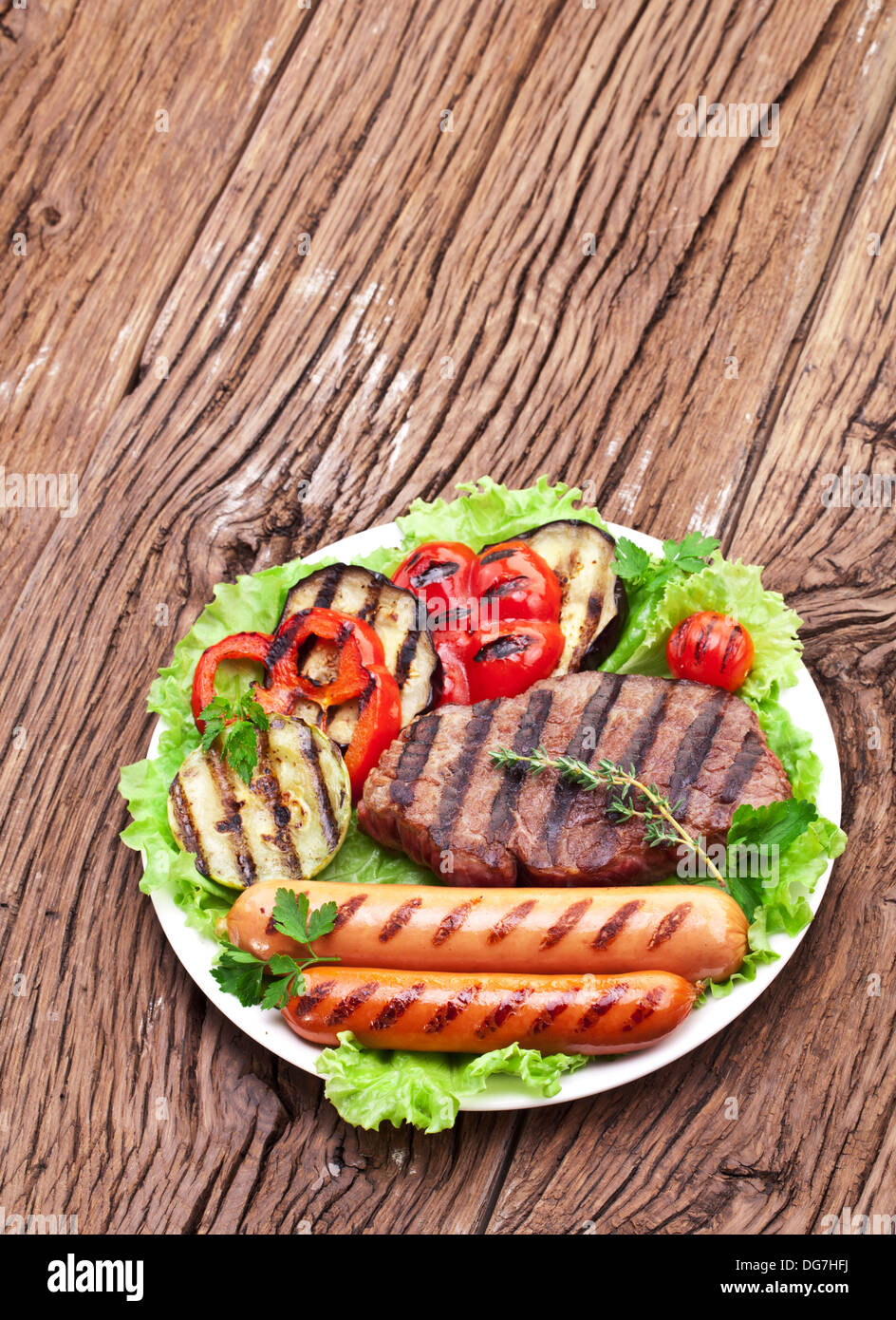 Bistecca alla griglia,salsicce e verdure sopra le foglie di lattuga su un tavolo di legno. Foto Stock