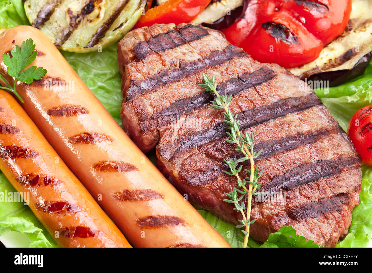 Bistecca alla griglia,salsicce e verdure sopra le foglie di lattuga su un tavolo di legno. Foto Stock