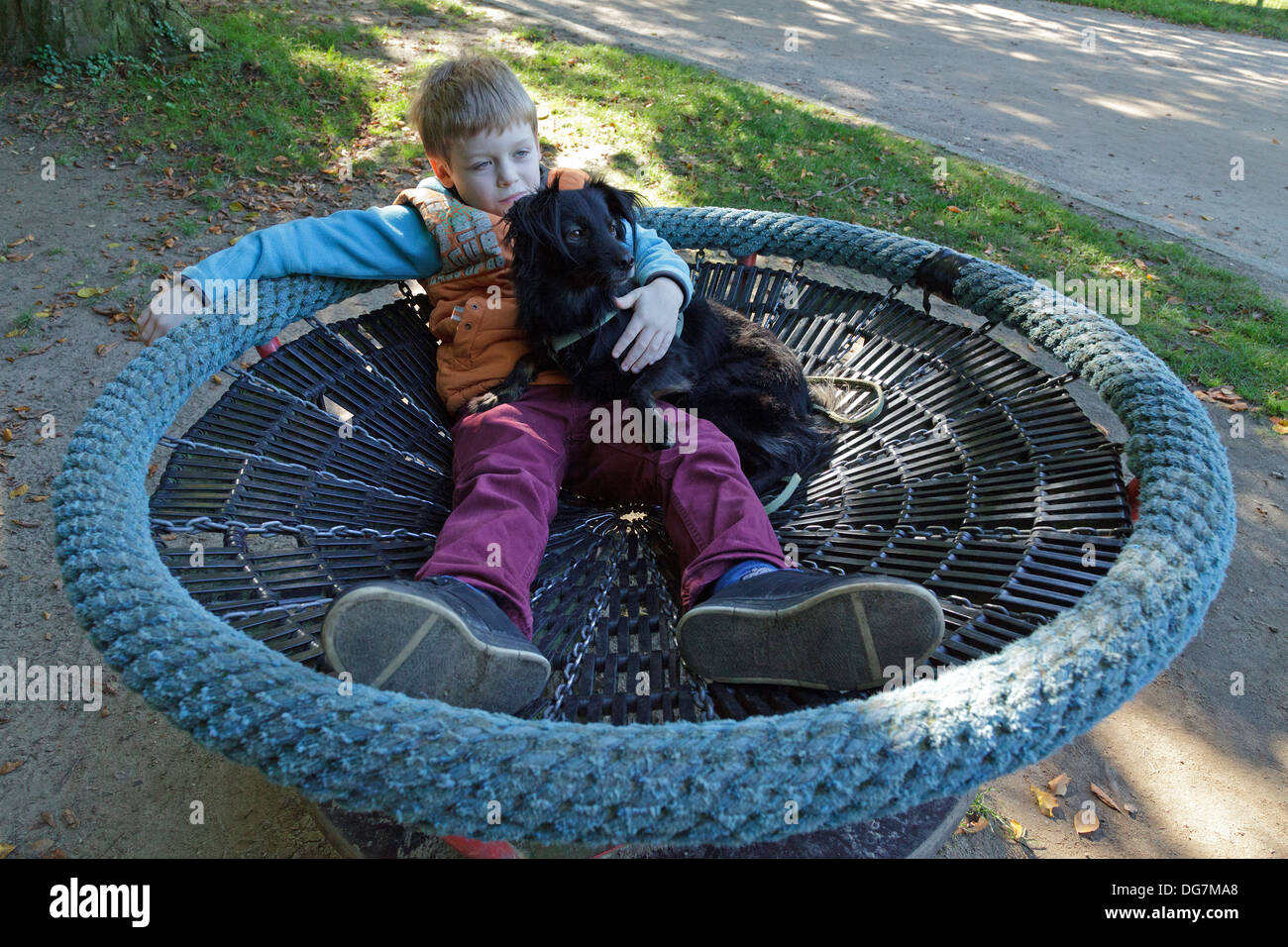 Little Boy reclinata su un trampolino cuddling il suo cane Foto Stock