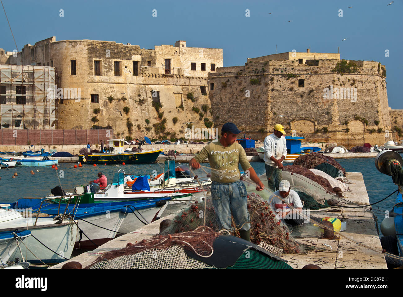 I pescatori riassettavano le reti in barca al di fuori del porto di cinta muraria medievale, Gallipoli, Puglia, Italia Foto Stock