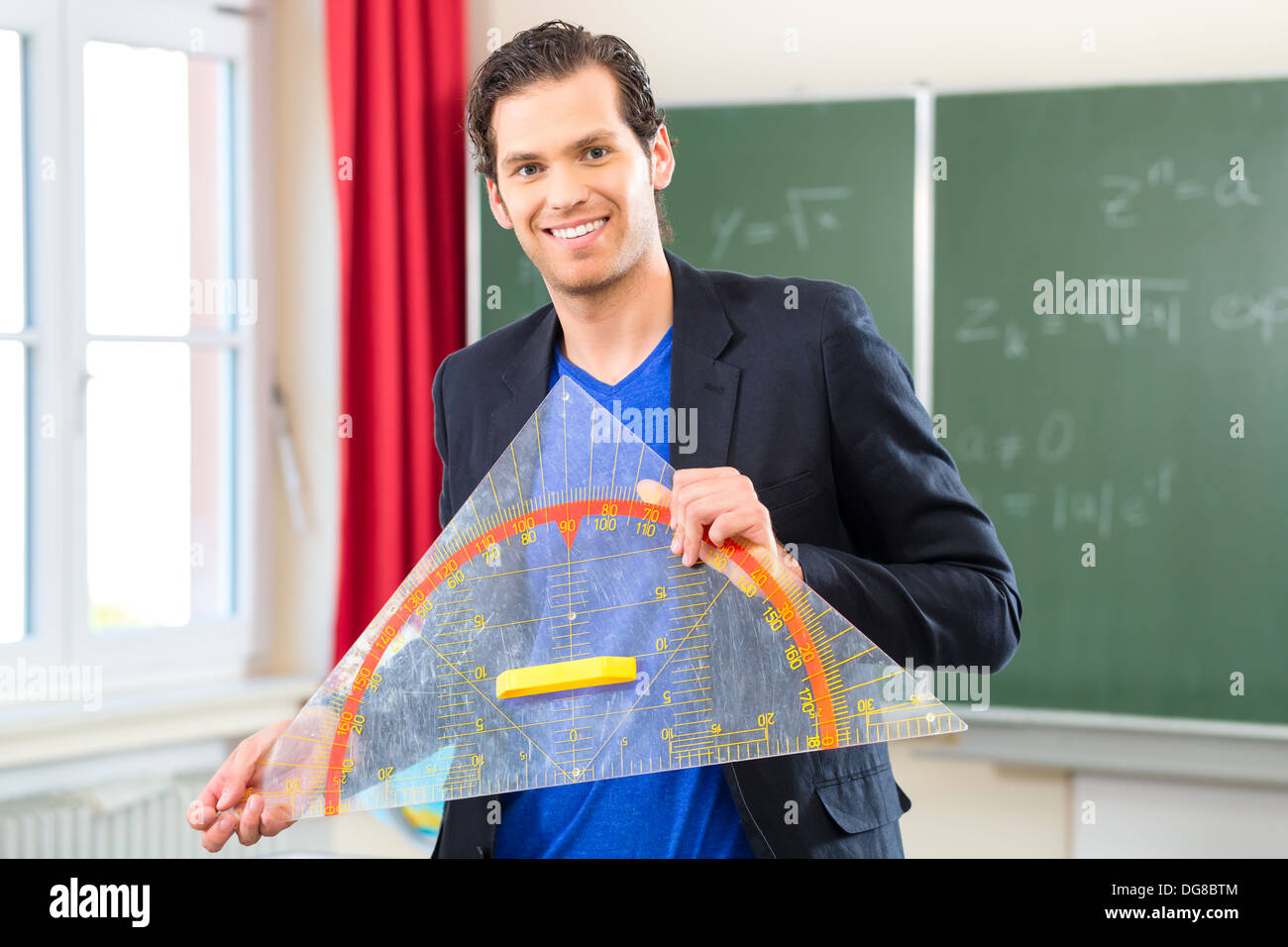 Insegnante o docente nella scuola in possesso di un triangolo geometria di fronte a una lavagna nella classe della scuola Foto Stock