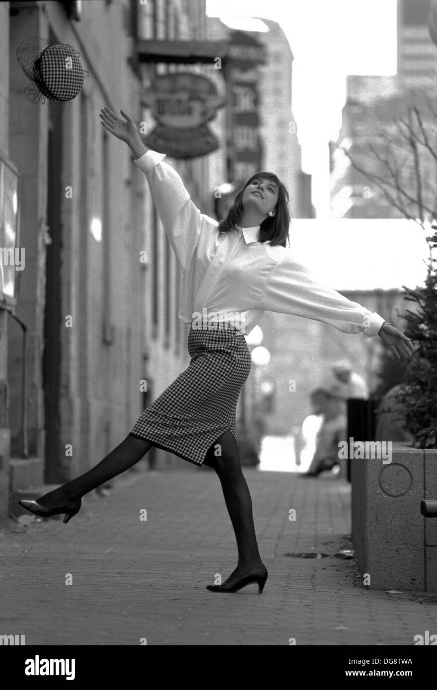 B&W fashion shot che mostra una giovane donna di gettare il suo cappello in aria. Foto Stock