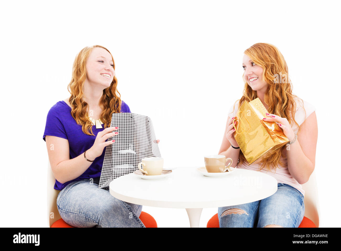 Felice redhead le donne sedute a un tavolo da caffè con le borse della spesa su sfondo bianco Foto Stock