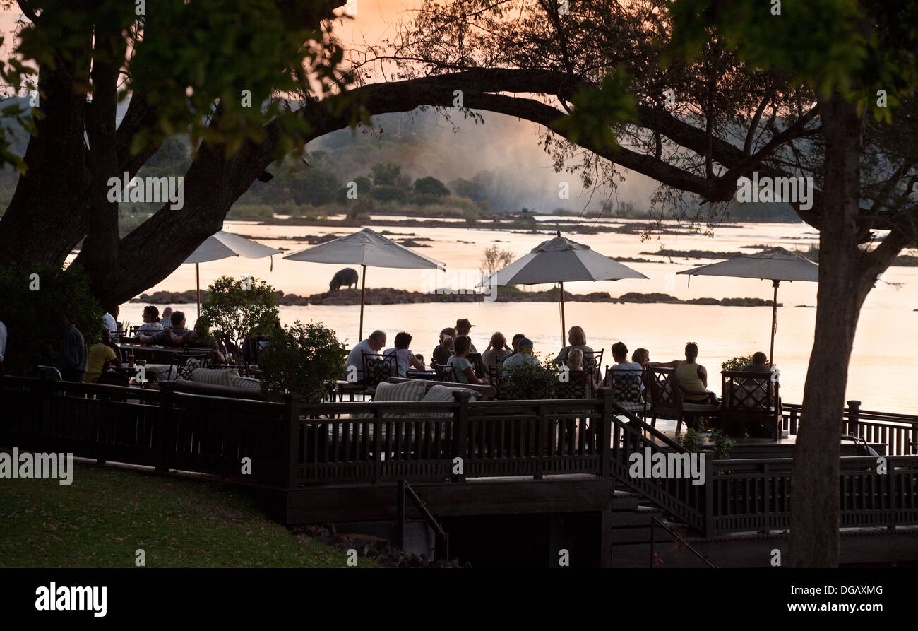 Gli ospiti sulla veranda al tramonto guardando il tramonto sul fiume Zambesi con Ippona, Royal Livingstone Hotel, Zambia Africa Foto Stock