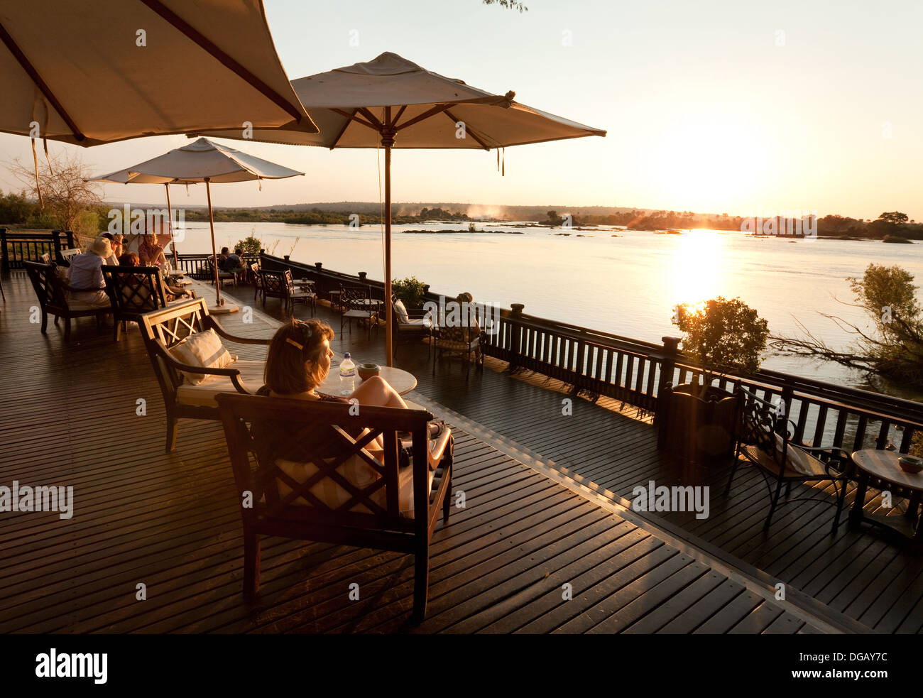 Gli ospiti sulla veranda al tramonto guardando il tramonto sul fiume Zambesi, Royal Livingstone Hotel, Zambia Africa Foto Stock