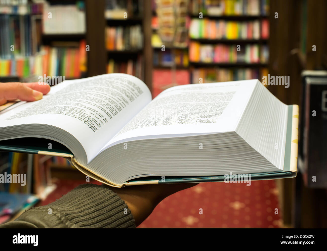 Mano che tiene aperto libro in una libreria. Molti libri sullo sfondo Foto Stock