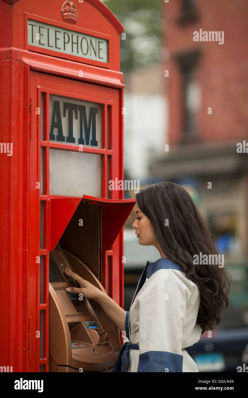 Metà donne adulte utilizzando contanti macchina in un telefono pubblico box Foto Stock