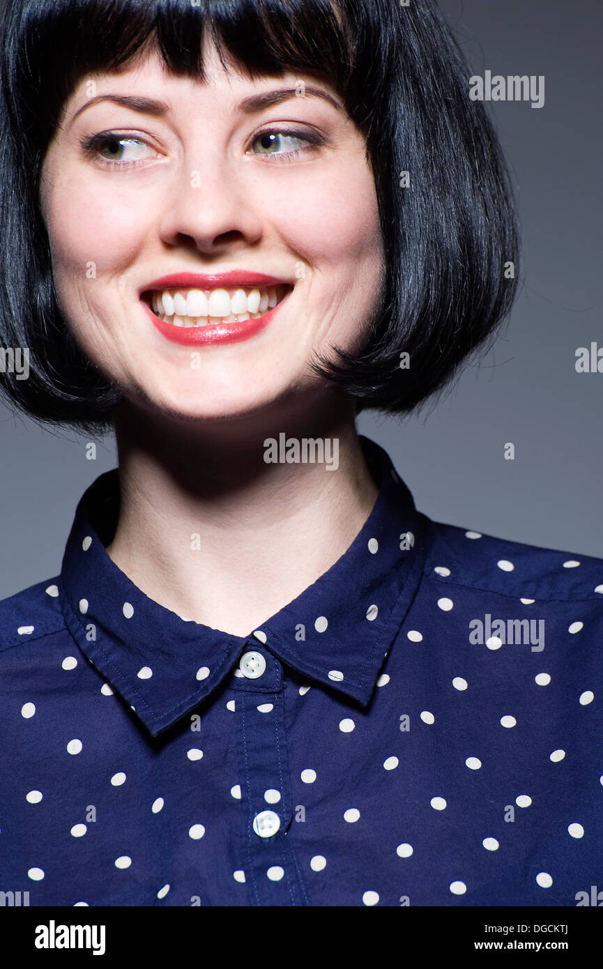 Giovane donna in blue spotted camicetta guardando lontano, sorridente Foto Stock