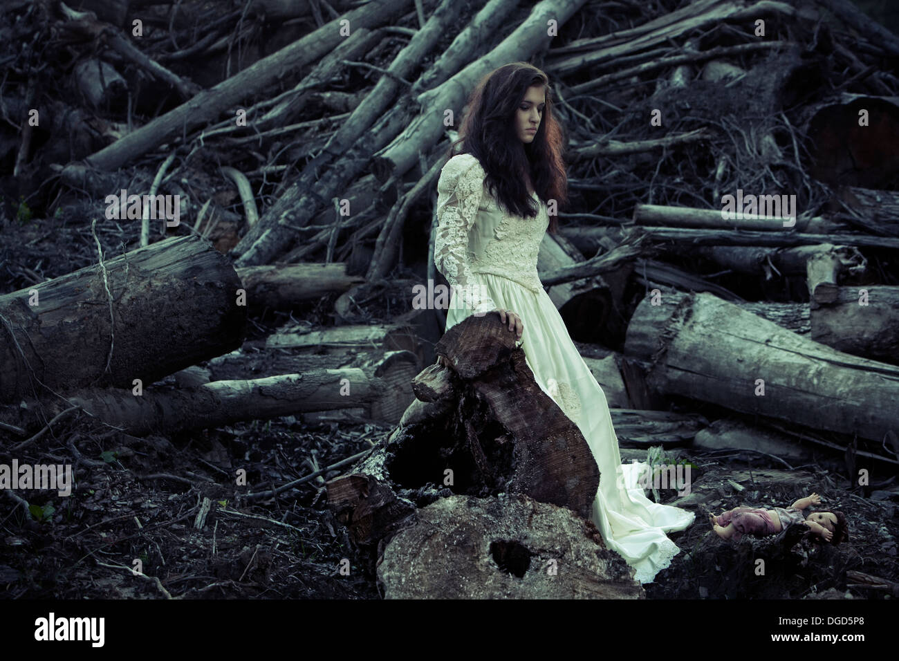 La donna in un antico edificio di abito da sposa davanti a tagliare gli alberi e creepy doll Foto Stock