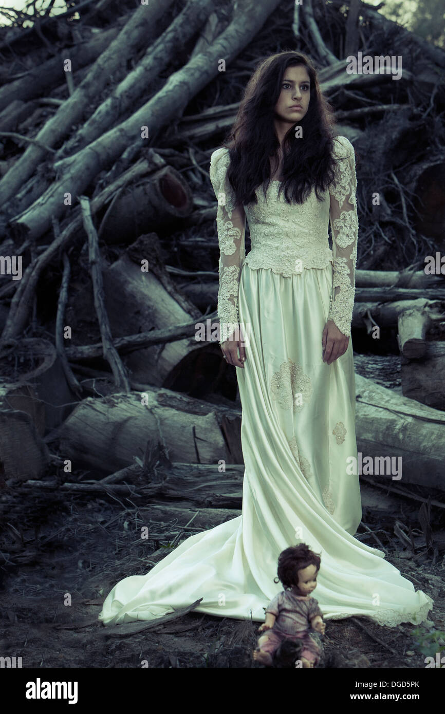 La donna in un antico edificio di abito da sposa con tagliare gli alberi e creepy doll Foto Stock