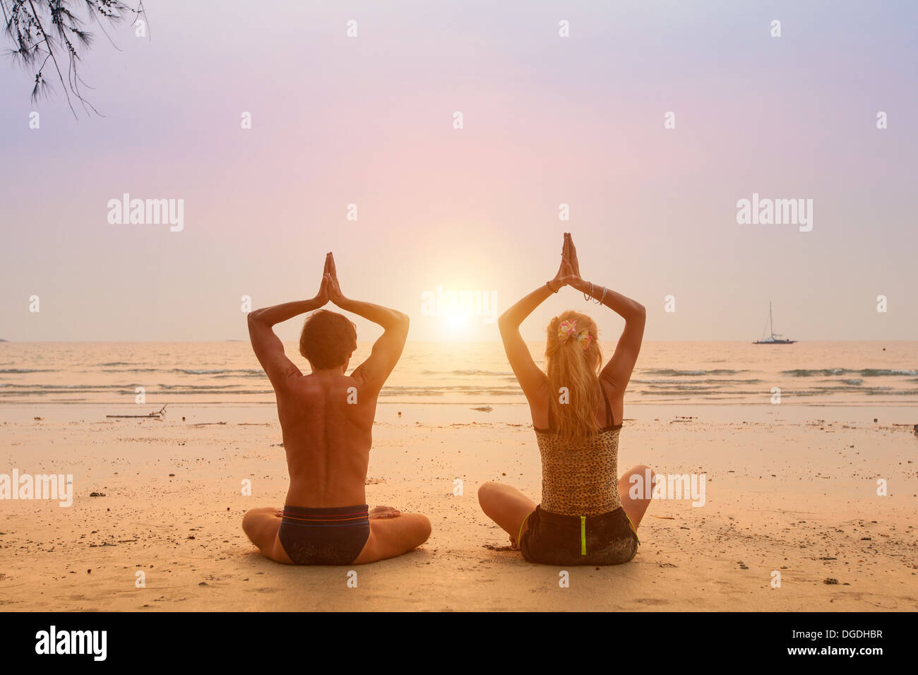 Coppia giovane seduto sulla spiaggia del mare nella posizione del loto al tramonto. Foto Stock