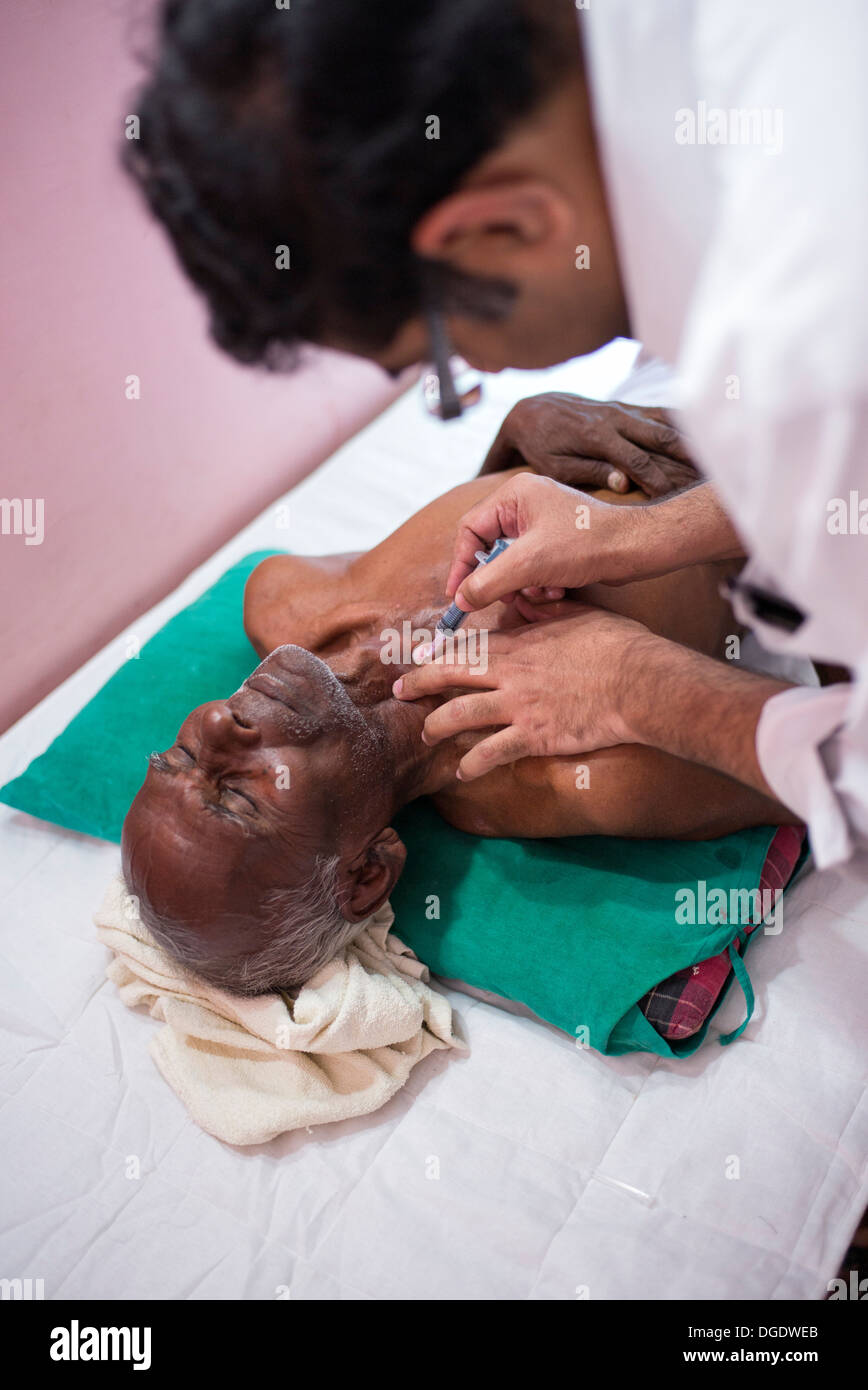 L'aspirazione con ago fine patologo estrazione delle celle in un grumo di un paziente di sesso maschile a Sathya Sai Mobile Ospedale outreach Foto Stock