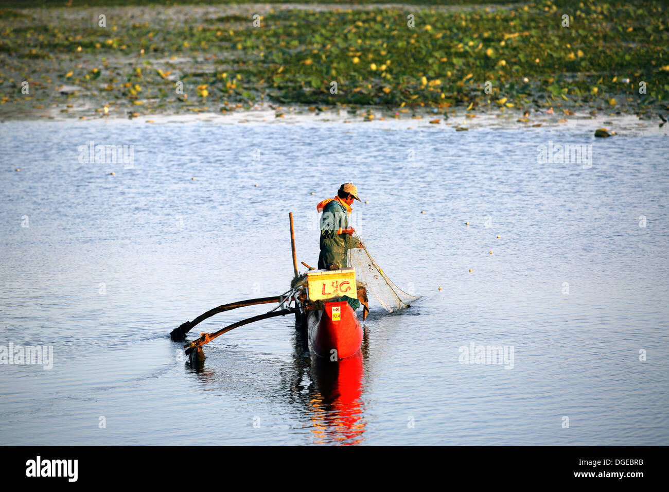 Lone dello Sri Lanka pescatore nel controllo della sua rete da pesca dalla sua semplice canoa outrigger sulla laguna di Arugam Foto Stock