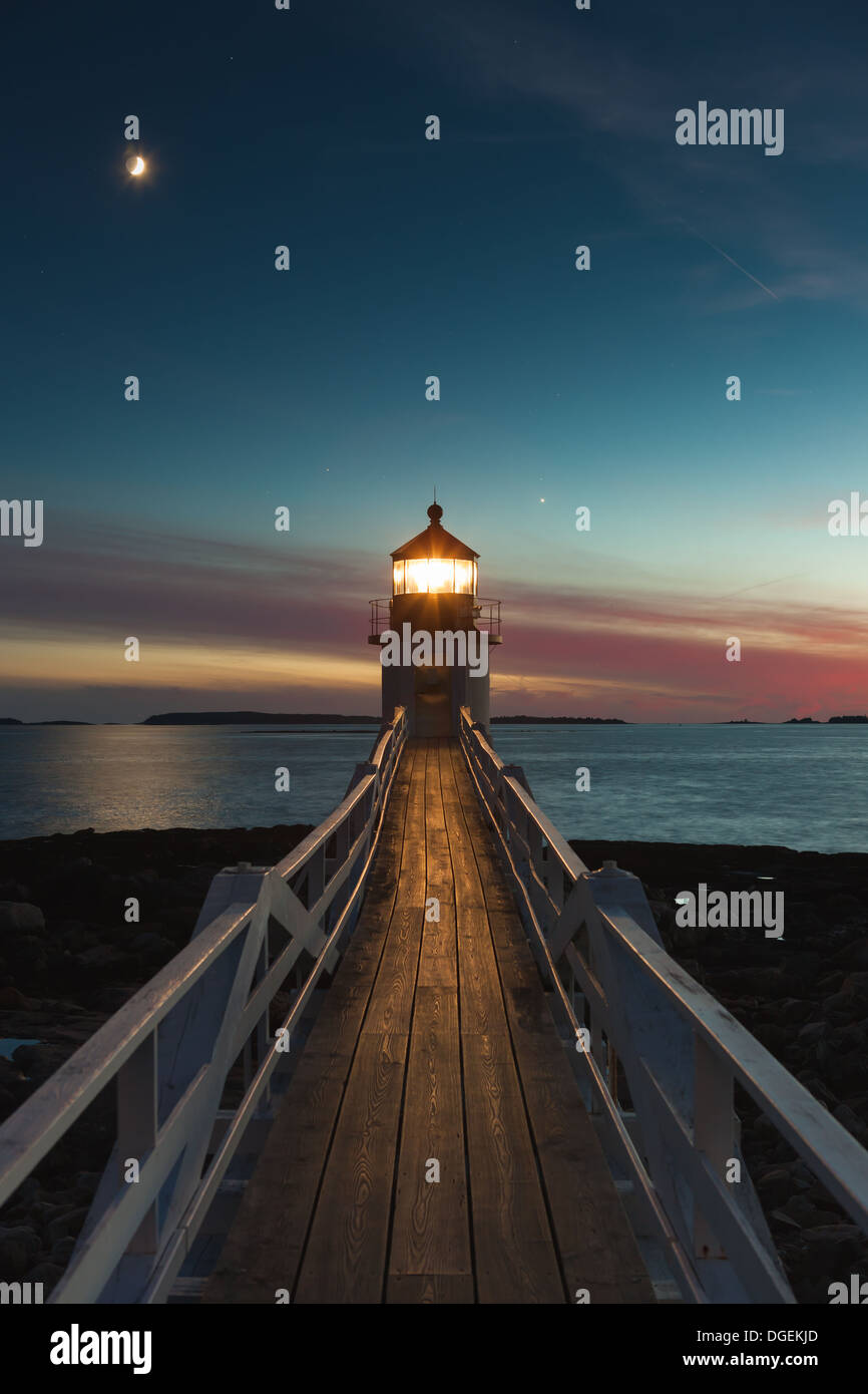 Marshall Point Lighthouse brilla nel cielo della sera sotto una luna crescente sulla porta Clyde Porto di Port Clyde, Maine. Foto Stock