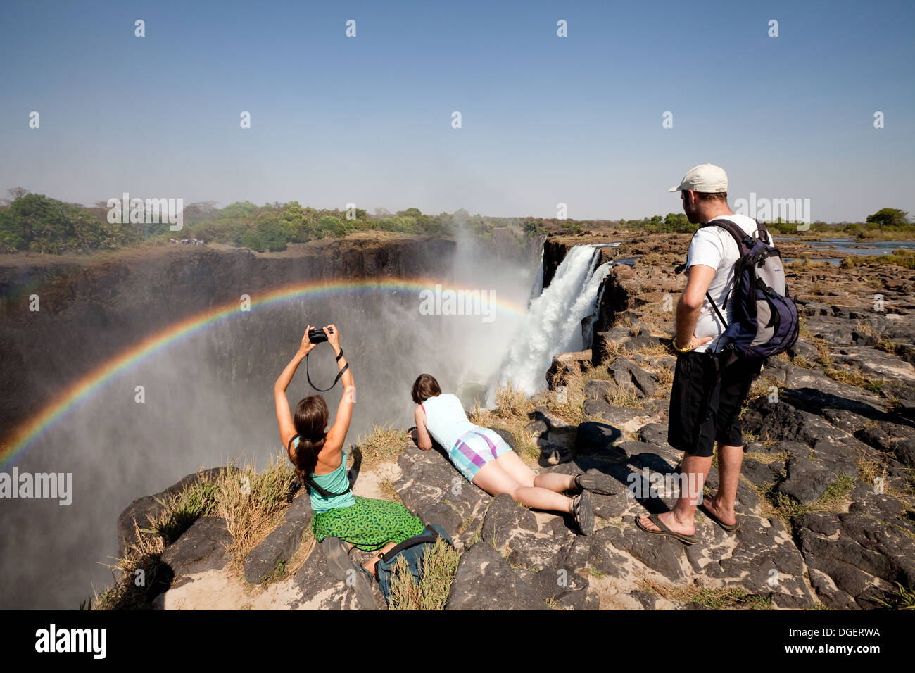 Tre turisti in cerca a Victoria Falls e rainbow da Livingstone Island, Zambia africa Foto Stock