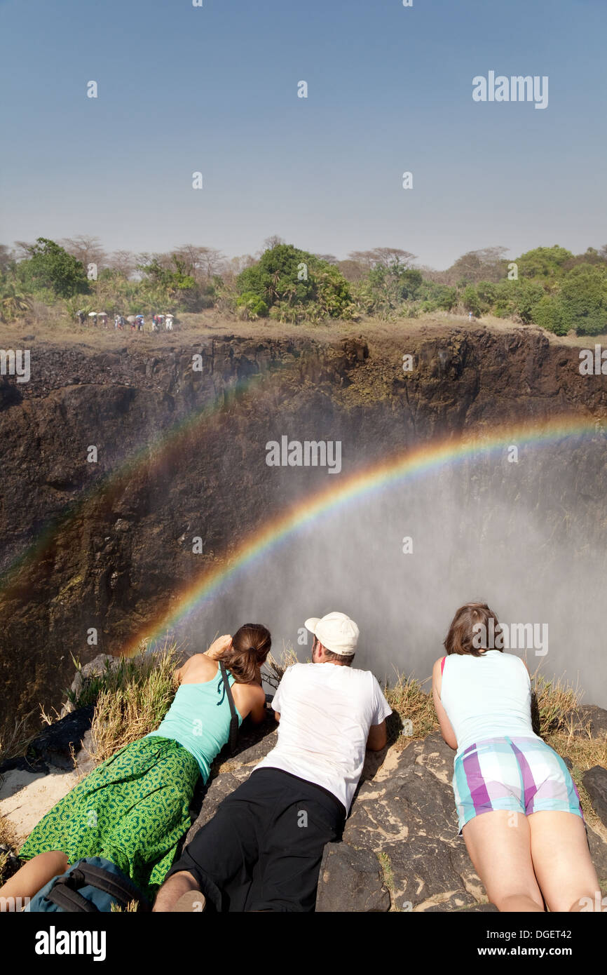 Victoria Falls nello Zambia, tre turisti su isola di Livingstone, Zambia guardando l'arcobaleno e il Victoria Falls, Africa Foto Stock