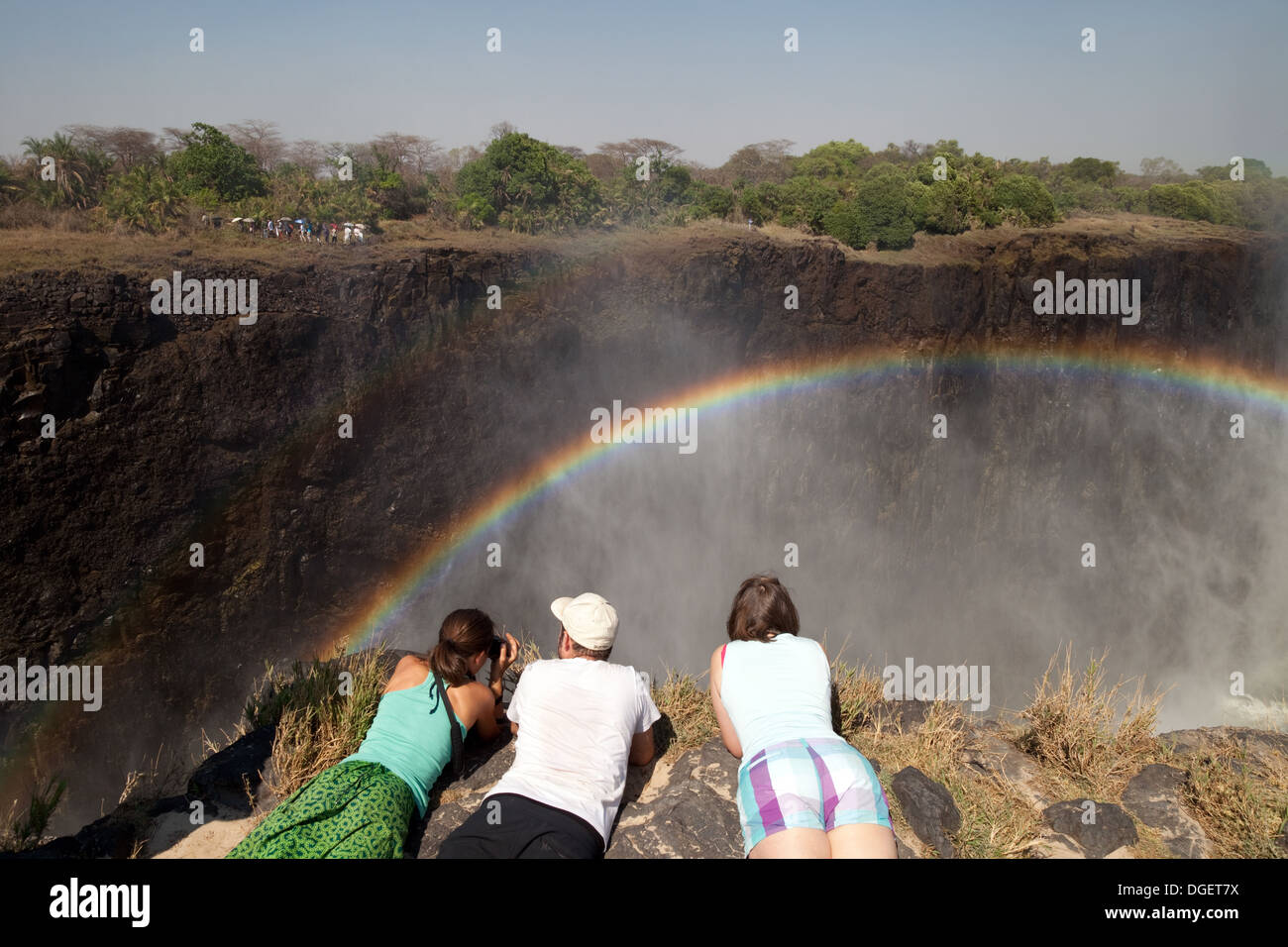 Victoria Falls nello Zambia, tre turisti su isola di Livingstone, Zambia guardando l'arcobaleno e il Victoria Falls, Africa Foto Stock