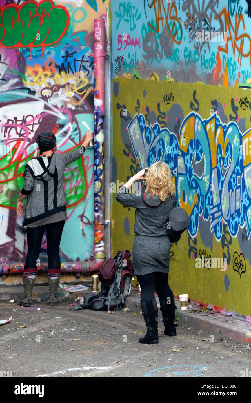 Giovane donna graffiti di spruzzatura sulla parete di strada con un amico a fotografare la scena Foto Stock