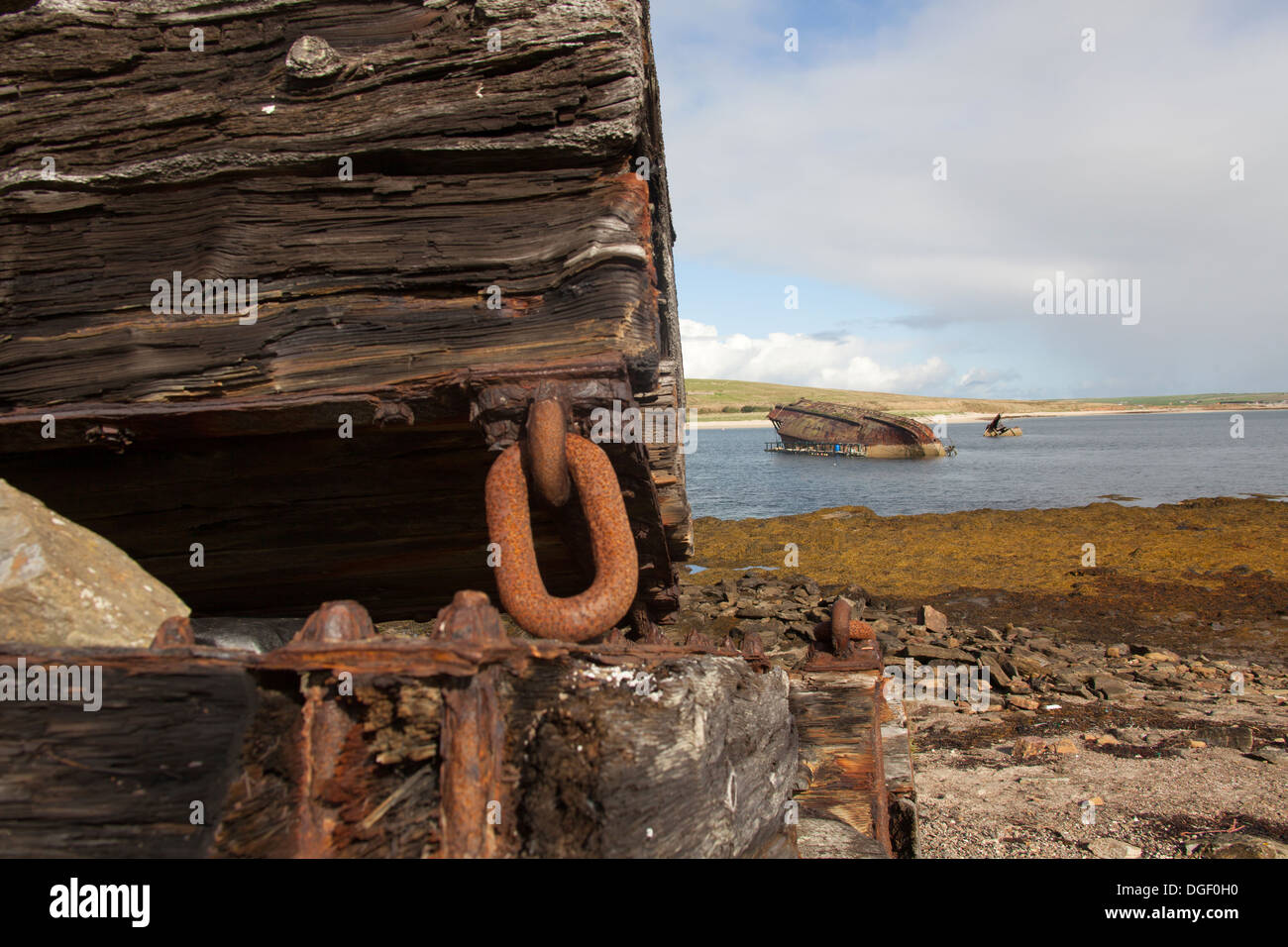 Isole di Orkney, Scozia. I detriti sulla riva adiacente alla barriera di Churchill numero 3 con un blockship in background. Foto Stock