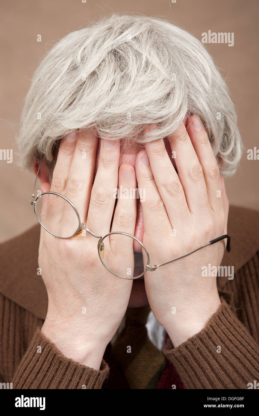 Vecchio vecchio dai capelli grigi, con le mani che coprono il viso, tenendo anche i suoi vetri da lettura. Foto Stock