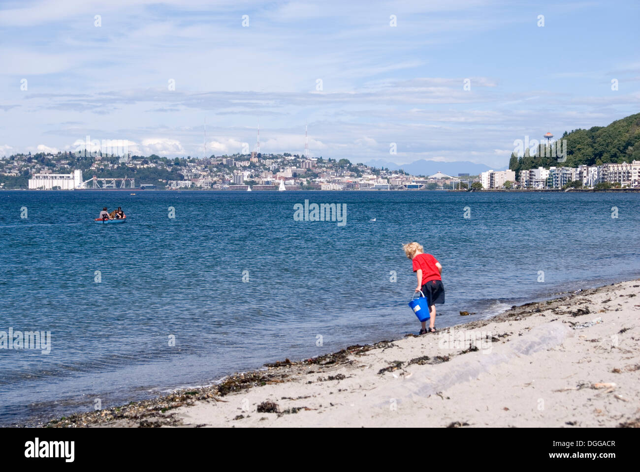 Giovane ragazzo giocando sulla spiaggia di Alki e un paio di gite in barca nella Baia di Elliott, Alki, West Seattle, Stati Uniti d'America Foto Stock