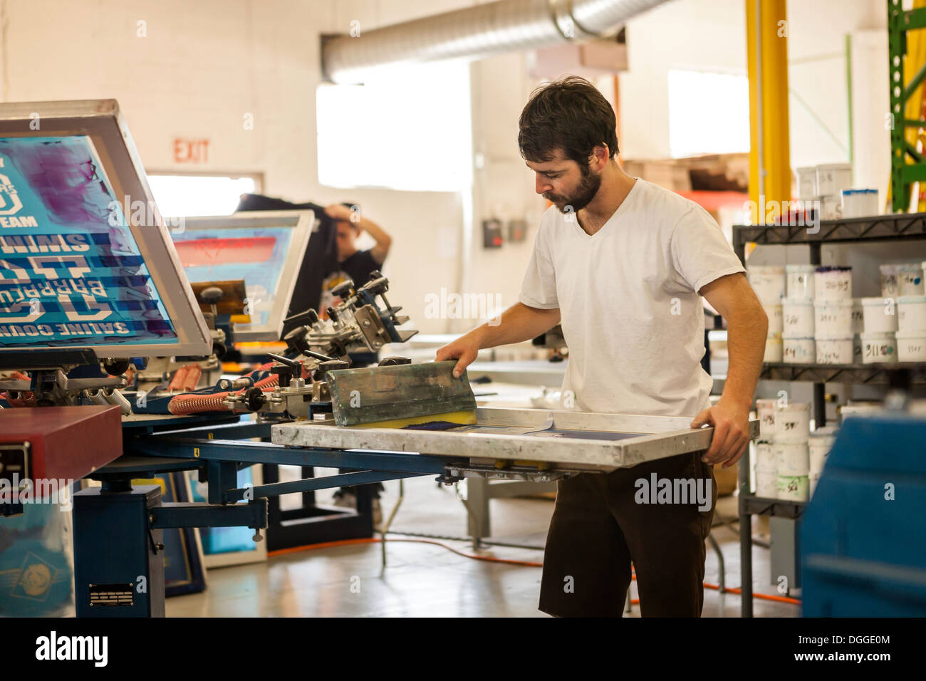 Lavoratore premendo l'inchiostro sul telaio nella stampa serigrafica workshop Foto Stock