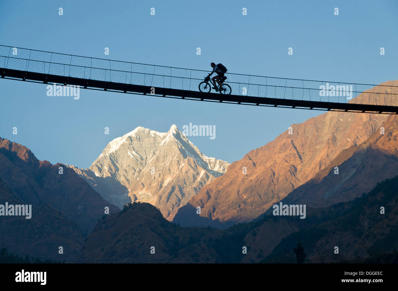 Ciclista attraversando un ponte di sospensione oltre la Kali Ghandaki Valley, Nilgiri Mountain nel retro, Tatopani, Regione di Annapurna, Nepal Foto Stock