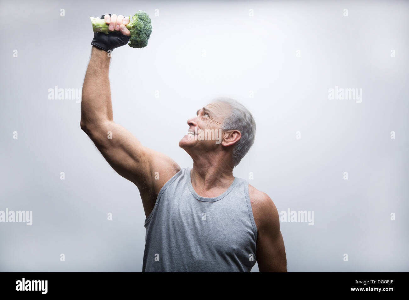 Senior uomo che guarda verso l'alto e sollevamento broccoli Foto Stock