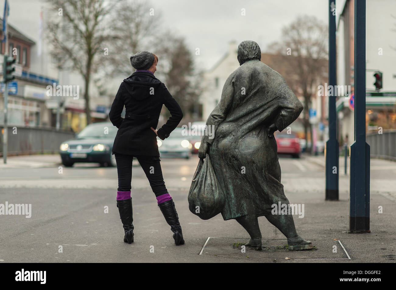 Giovane donna in piedi accanto a una statua di bronzo in zona pedonale, Grevenbroich, Renania settentrionale-Vestfalia Foto Stock