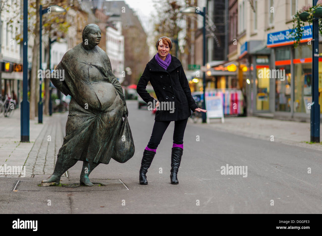 Giovane donna in piedi accanto a una figura di bronzo nella zona pedonale, Grevenbroich, Renania settentrionale-Vestfalia Foto Stock