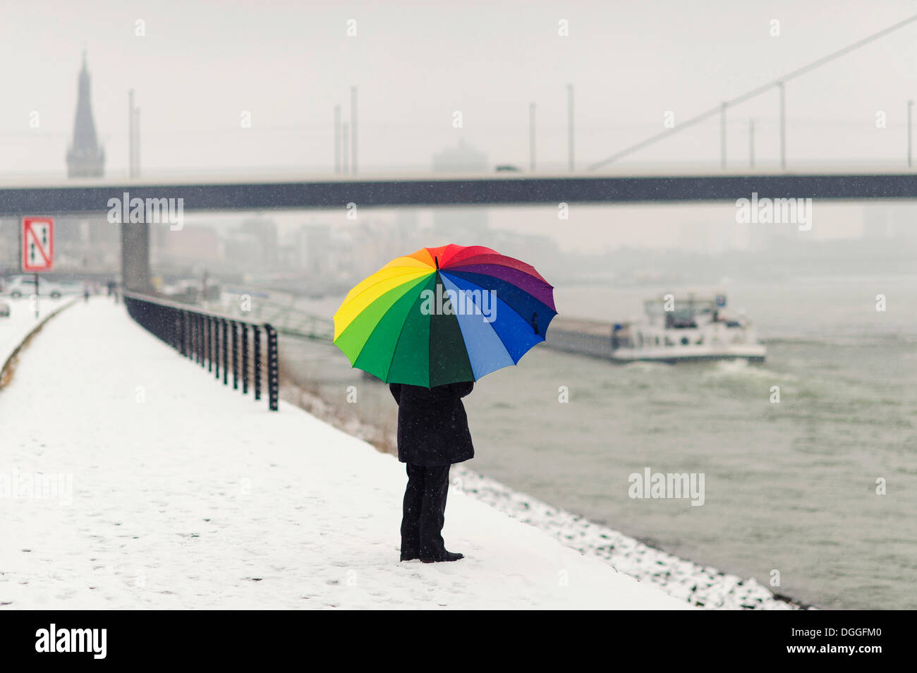 Donna in piedi con un ombrello coloratissimo in inverno sulla banca del fiume Reno, Düsseldorf, Renania Foto Stock