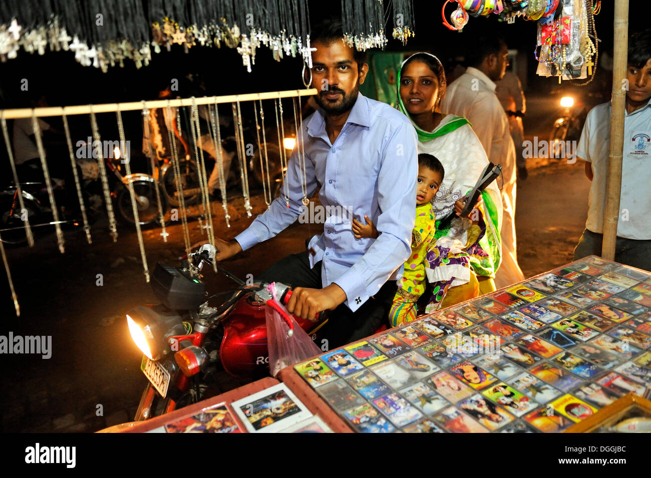 Famiglia giovane su una moto acquisto di un crocifisso in legno in una fase di stallo che offrono prodotti di cristiana, quartiere cristiano di Youhanabad Foto Stock