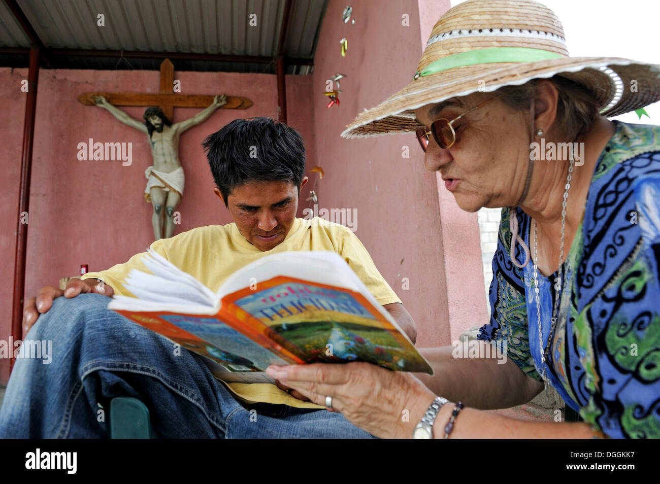 Donna anziana con cappello per il sole di insegnamento di una giovane migrante a leggere in un rifugio per i paesi dell'America Latina migranti, Ixtepec, Oaxaca, Messico Foto Stock