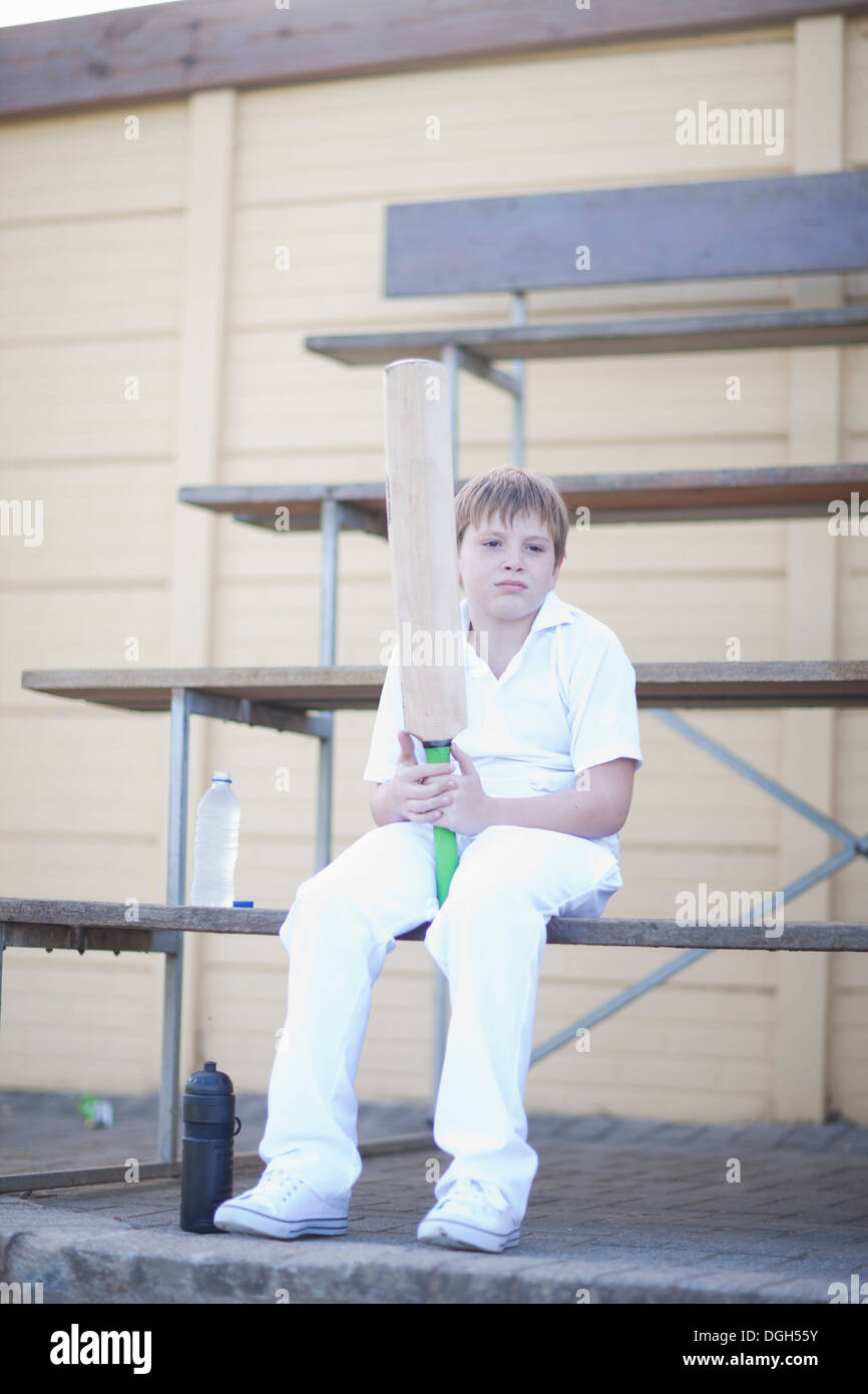 Ragazzo holding cricket bat seduti sulle gradinate Foto Stock