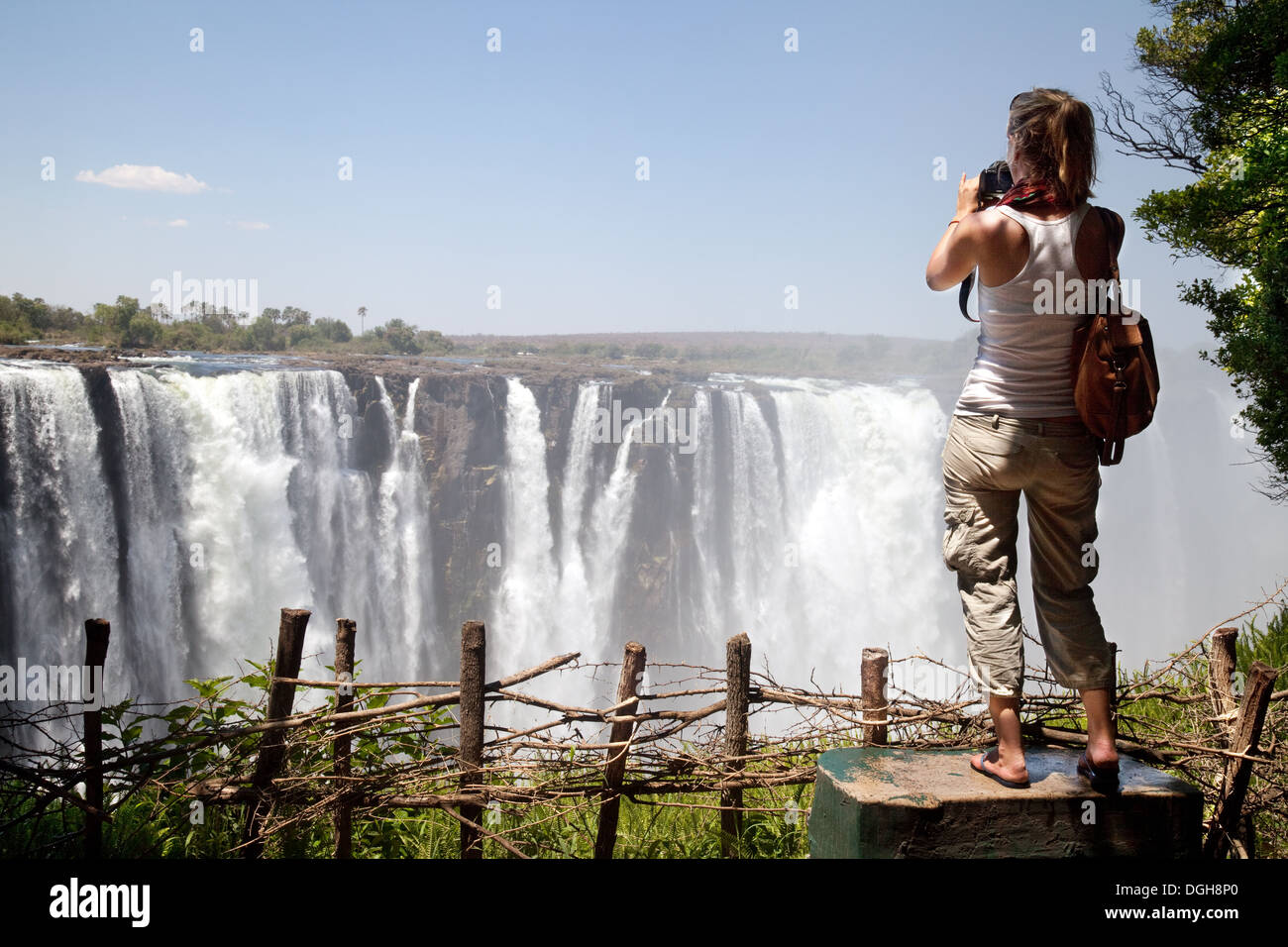 Viaggio solo; giovane donna turistica scattare una foto delle Cascate Vittoria, cataratta principale, dal Parco Nazionale delle Cascate Vittoria, Zimbabwe, Africa Foto Stock